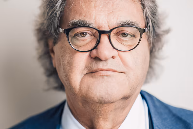Porträt eines älteren Mannes mit Brille und grauem Haar in blauem Businessanzug vor neutralem Hintergrund