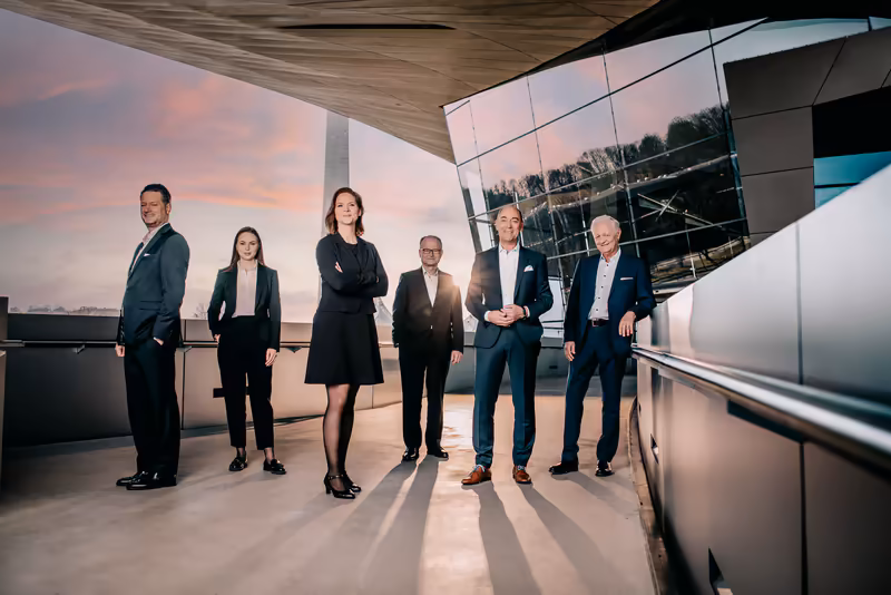 Sechsköpfiges Business-Team in formaler Kleidung auf moderner Dachterrasse bei Sonnenuntergang