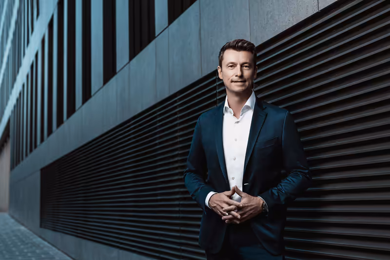 Mann in dunklem Anzug und weißem Hemd vor moderner Architektur mit Metalljalousien, professionelles Business-Porträt