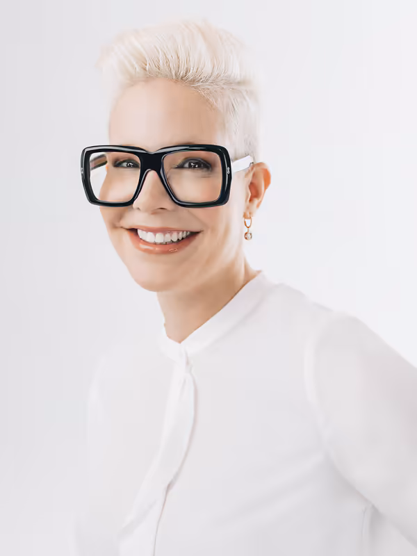 Frau mit weißem Haar und Brille, strahlend lächelnd, weißes Hemd, Business-Porträt vor hellem Hintergrund