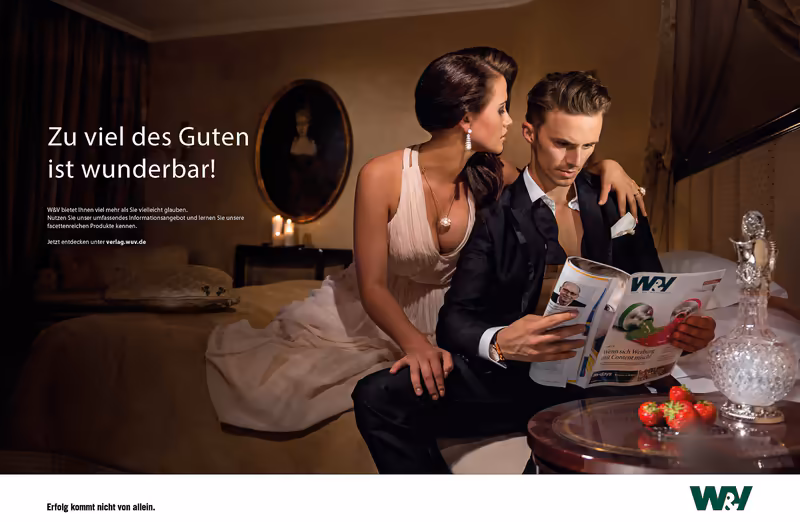 Zwei Personen in eleganter Kleidung sitzen auf Bett, Mann liest Magazin, warme Hotelzimmer-Atmosphäre