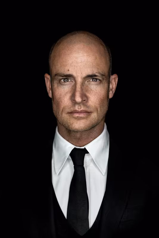 Mann im Business-Portrait mit weißem Hemd und schwarzer Krawatte vor dunklem Hintergrund, direkter Blick, professionelle Headshot-Fotografie