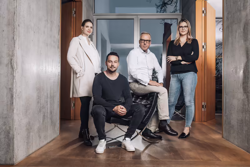 Vier Personen im modernen Büro, selbstbewusste Teamaufnahme in entspannter Pose vor Glastüren