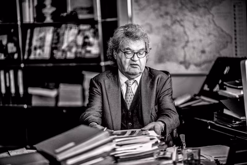 Älterer Mann im Anzug mit Brille arbeitet konzentriert an Dokumenten am Schreibtisch in modernem Büro