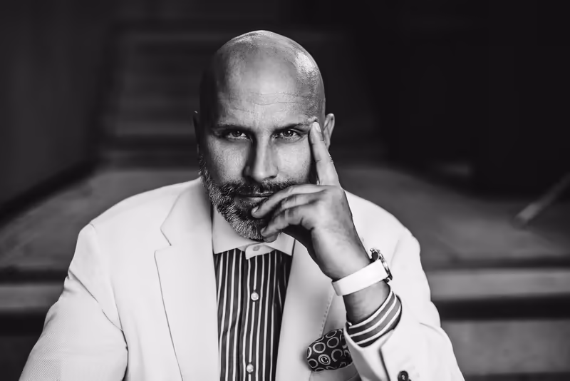 Mann mit Bart in hellem Blazer und gestreiftem Hemd, nachdenkliche Pose mit Hand am Gesicht, Schwarzweiß-Porträt