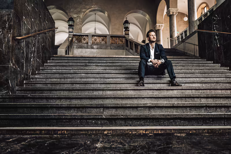 Geschäftsmann sitzt auf Treppe in klassischer Architektur, nachdenkliche Pose, Business-Portrait