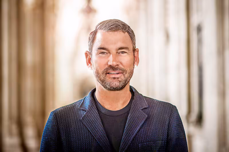 Mann mit Bart in dunklem Blazer, freundlicher Blick, unscharfer heller Hintergrund, Business-Portrait