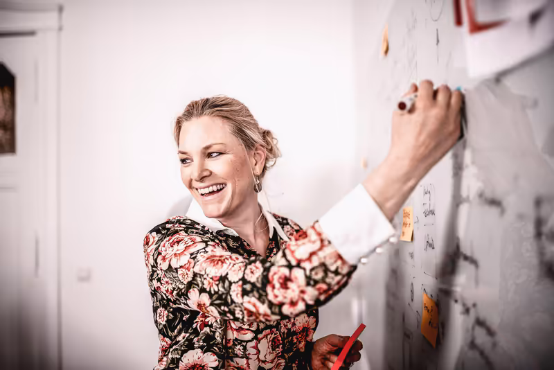 Frau schreibt lächelnd Notizen an Whiteboard, Business-Portrait im modernen Büro