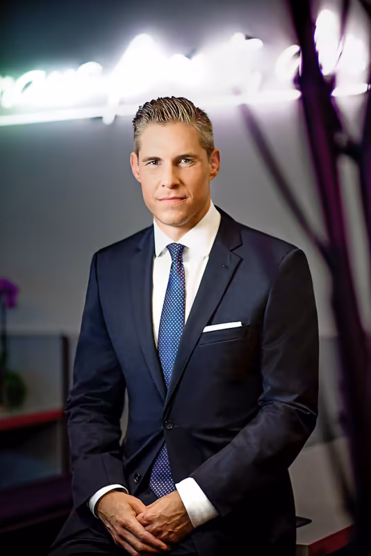 Mann in dunklem Anzug und blauer Krawatte vor modernem Neon-Hintergrund, Business-Portrait