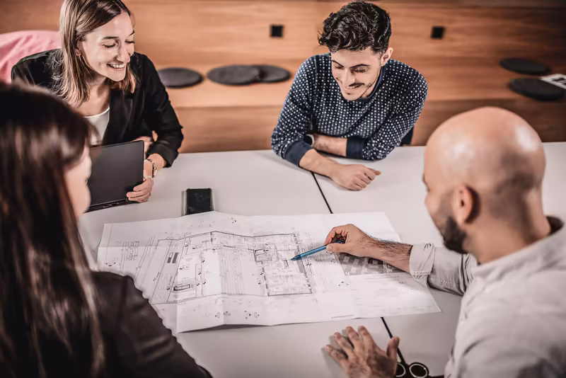 Geschäftsteam bespricht Architekturpläne an Konferenztisch, kollegiale Atmosphäre