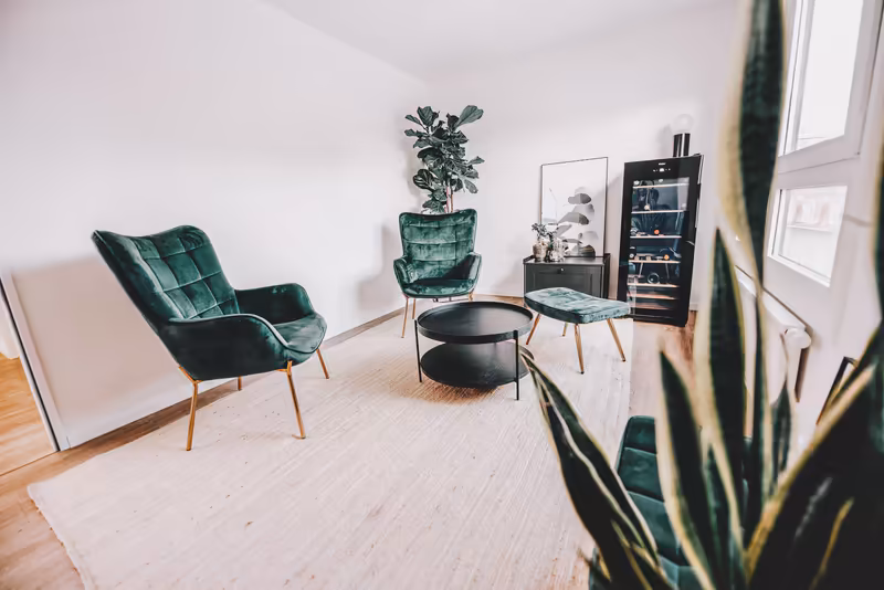 Modernes Büro-Wartezimmer mit grünen Samtsessel, schwarzem Couchtisch, Pflanzen und minimalistischer Einrichtung