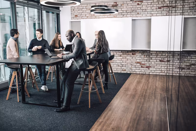 Geschäftsteam bei Besprechung an Stehtisch in modernem Büro mit Ziegelwand