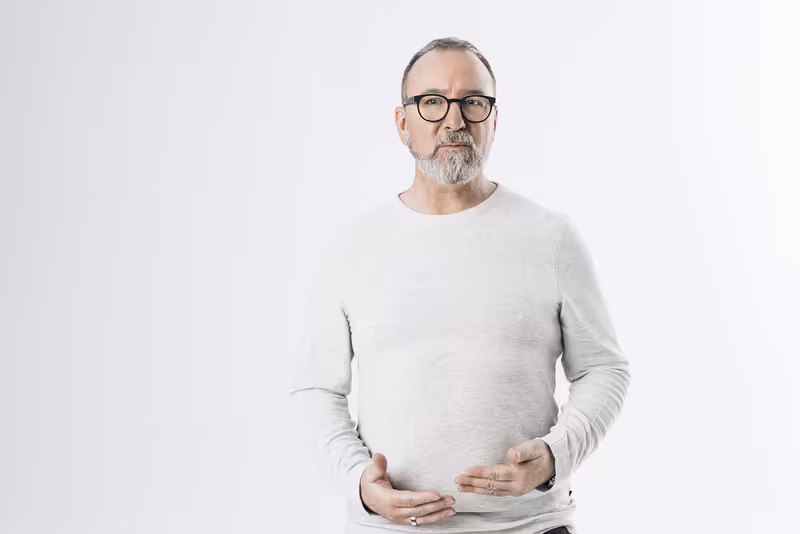 Mann mit Brille und Bart in hellem Langarmshirt vor neutralem Hintergrund, Business-Porträt