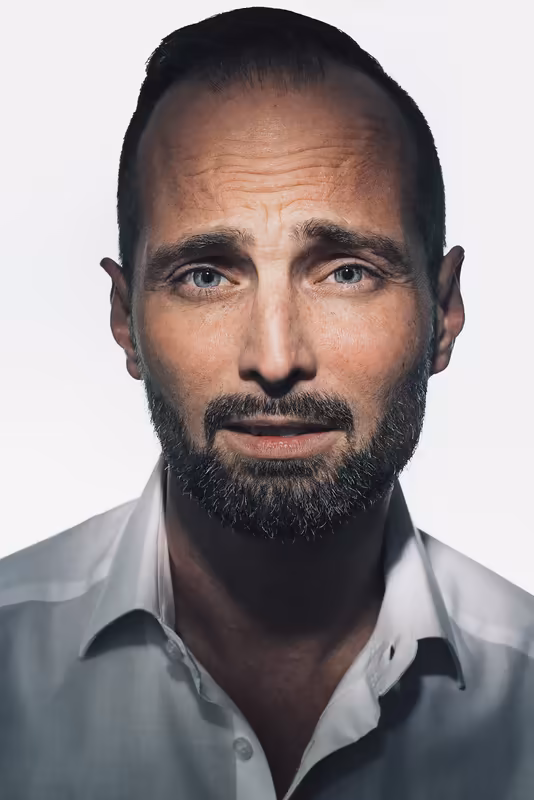 Mann mit Bart in weißem Hemd, ernsthafter Blick, Business-Portrait vor neutralem Hintergrund