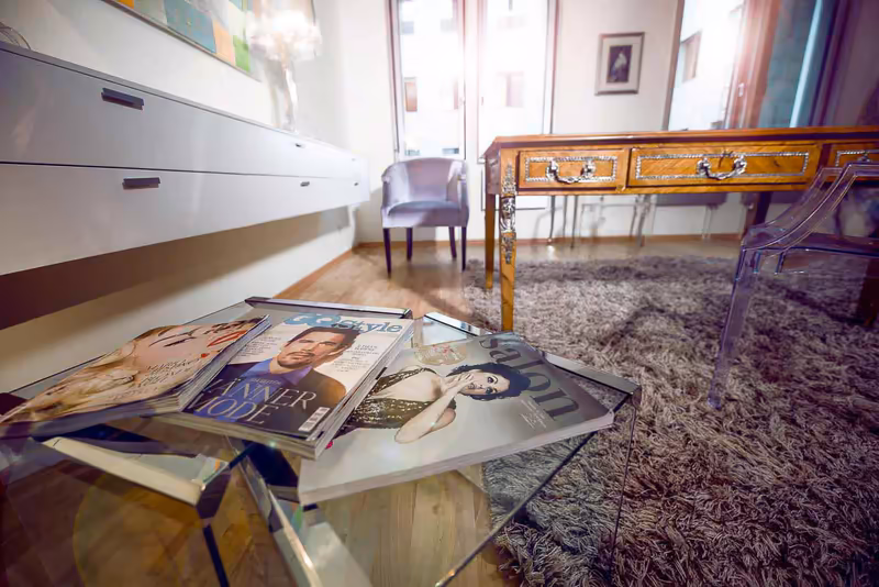 Elegantes Bürozimmer mit Magazinen auf Glastisch, modernem Schrank, Vintage-Schreibtisch und bequemem Sessel in warmer Atmosphäre