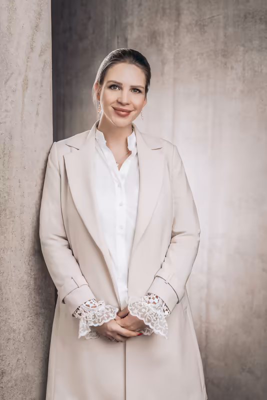 Geschäftsfrau in hellem Blazer und weißer Bluse vor grauer Betonsteinwand, selbstsicheres Portrait