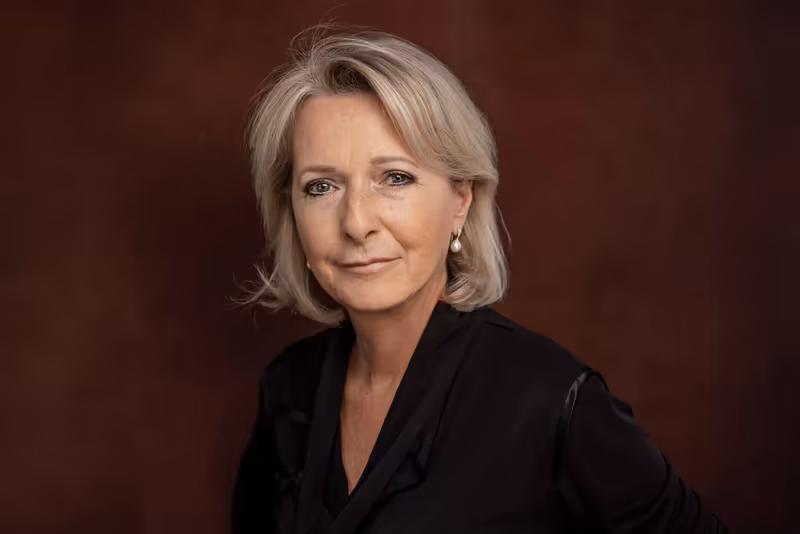 Porträt einer Frau mit grauem Haar in schwarzem Blazer vor burgunderfarbenem Hintergrund, professionelle Businessfotografie