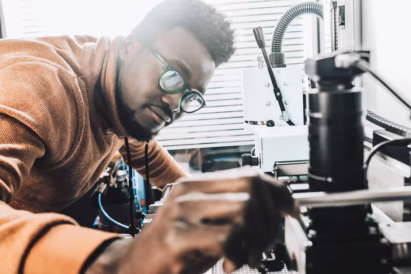 Techniker mit Schutzbrille arbeitet konzentriert an 3D-Drucker in modernem Werkstatt-Setting