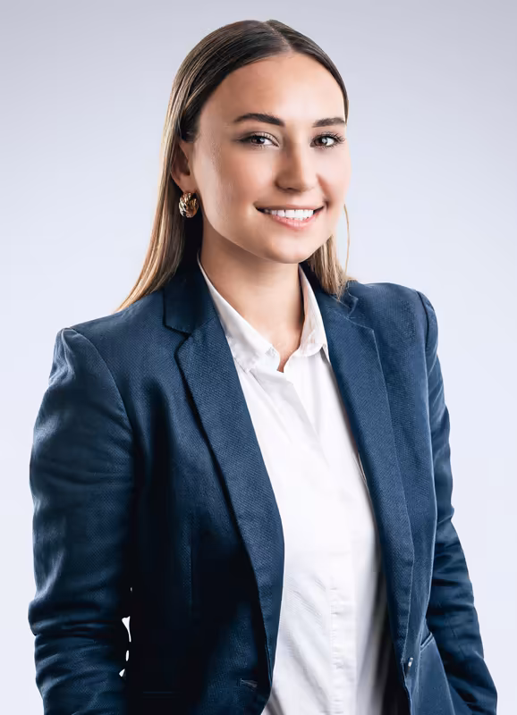 Frau im dunkelblauen Businessblazer und weißer Bluse, lächelnd, Porträt vor neutralem Hintergrund