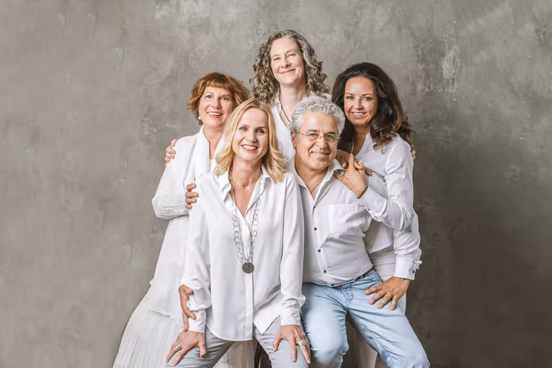 Fünf Geschäftsleute in weißen und hellen Hemden posieren lächelnd zusammen vor grauer Betonwand, Team-Portrait mit freundlicher Atmosphäre