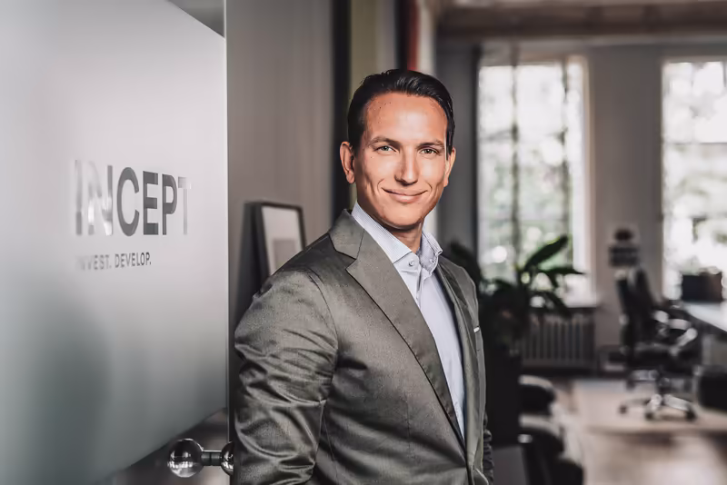 Geschäftsmann in grauem Anzug lehnt an Bürowand mit Logo, modernes Büro im Hintergrund