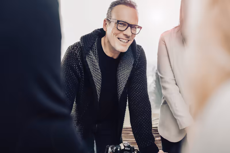 Mann mit Brille in Wollcardigan lächelt im Gespräch mit Geschäftspartnern, Business-Setting
