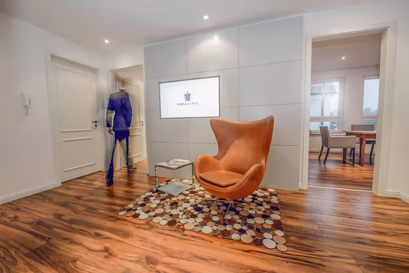 Modernes Büro mit Empfangsbereich, orangefarbenem Sessel, Holzboden, weißer Wandverkleidung und Person in blauem Anzug