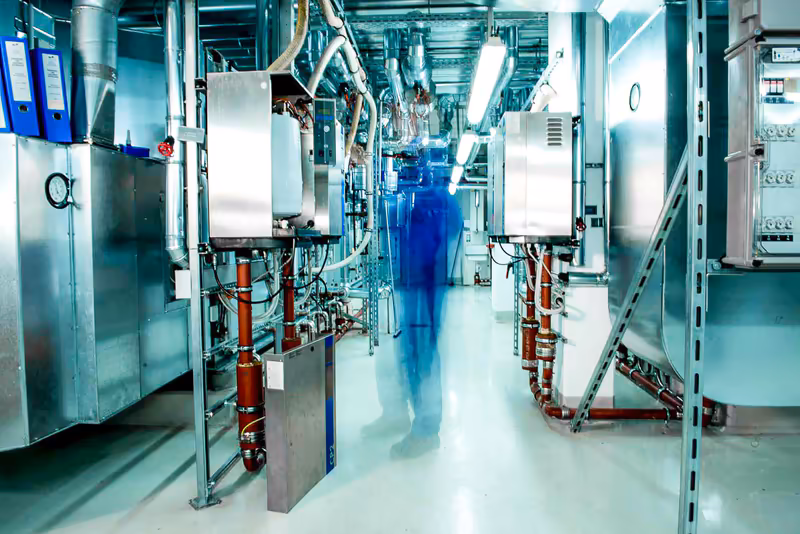 Technische Anlage mit Maschinen und Rohrsystemen in moderner Fabrikhalle, Person in Bewegung in futuristischer Industrieumgebung