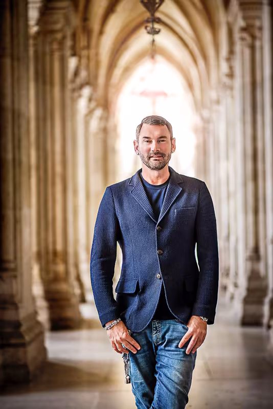 Mann in blauem Blazer und Jeans in gewölbter Arkaden-Halle, selbstbewusste Businessporträt-Pose