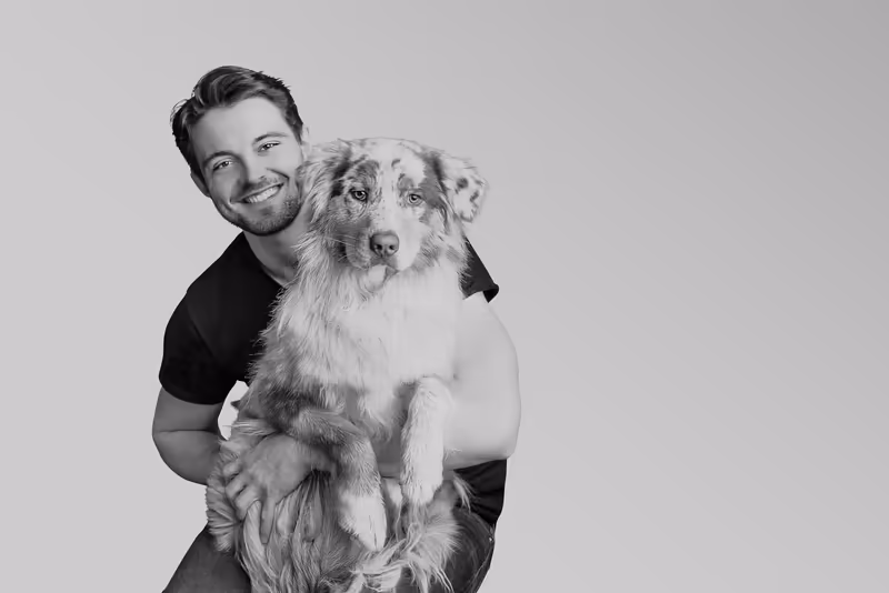 Mann in schwarzem Shirt haelt großen Hund, Schwarz-Weiß Portrait, freundliche Atmosphäre vor neutralem Hintergrund