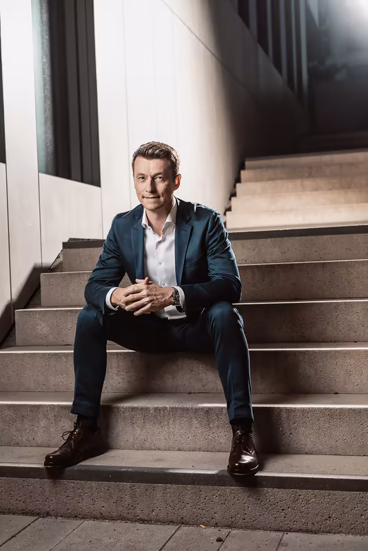 Mann in dunklem Anzug sitzt auf Betontreppe, moderne Architektur, selbstbewusstes Portrait