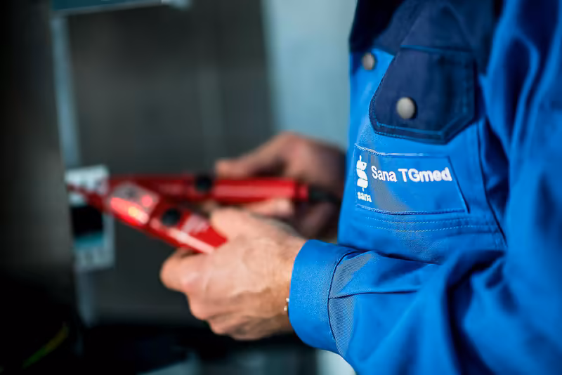 Techniker in blauer Arbeitskleidung haelt rote Messinstrumente in Hand, professionelle Werkstatt-Atmosphaere