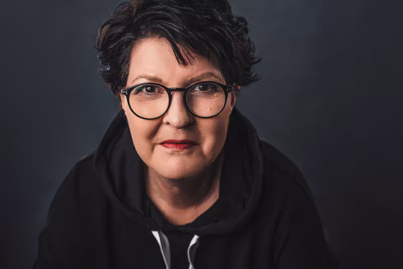 Porträt einer Frau mit Brille und schwarzem Hoodie vor grauem Hintergrund, professionelle Businessfotografie