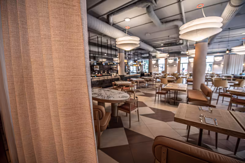 Modernes Restaurant-Interieur mit Textilvorhang, Holzstühlen, runden Tischen und Designer-Deckenleuchten in offenem Großraum