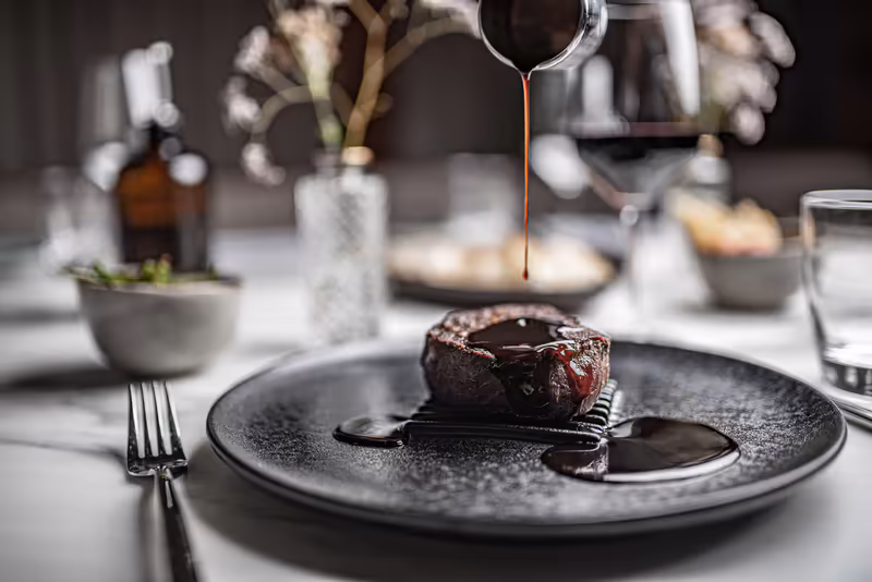 Gourmet-Schokoladendessert mit Sauce auf schwarzem Teller, elegantes Restaurantambiente mit Besteck und gedecktem Tisch