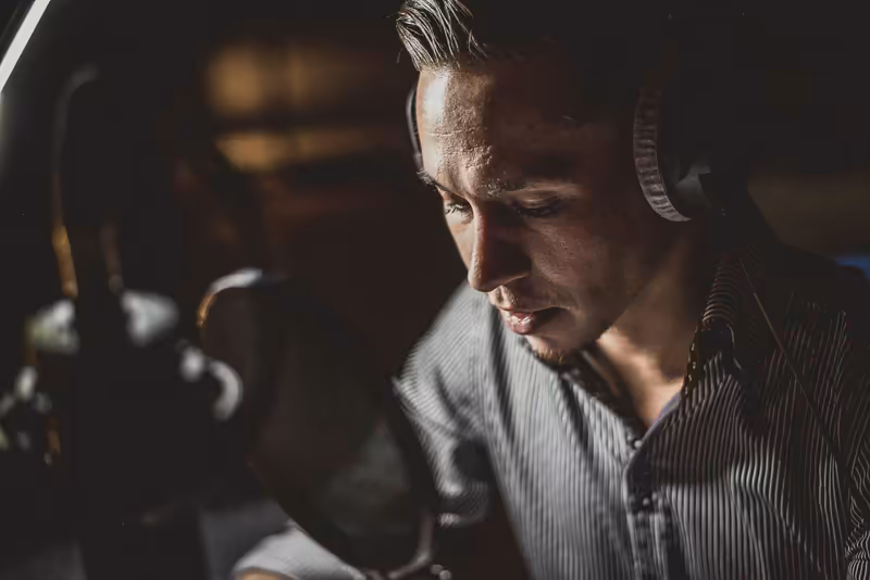 Mann mit Kopfhörern vor Mikrofon, konzentriert, Studio-Setting, Podcast oder Sprachaufnahme