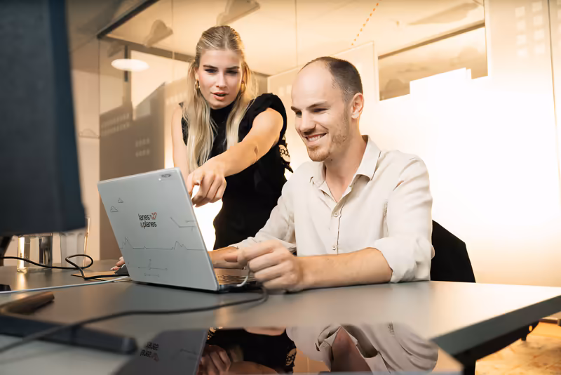 Zwei Geschäftsleute arbeiten gemeinsam am Laptop in modernem Büro, freundliche Zusammenarbeit und Teamwork