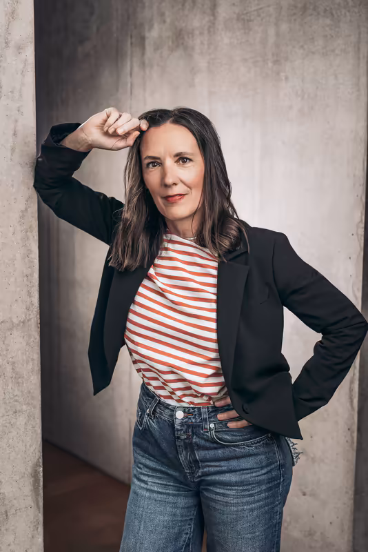 Frau in schwarzem Blazer und rot-weiß gestreiftem Shirt vor Betonwand, selbstbewusste Businessportraits