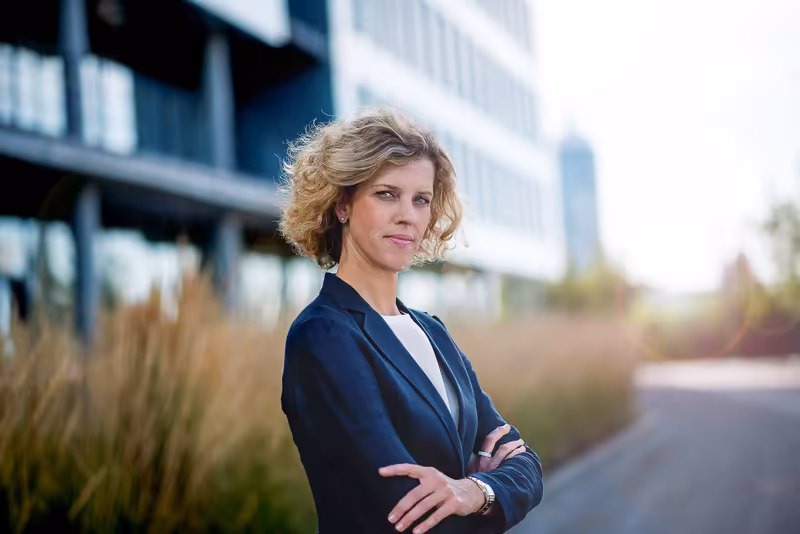 Frau in dunklem Blazer mit verschränkten Armen vor modernem Bürogebäude, selbstbewusste Business-Portraitfotografie