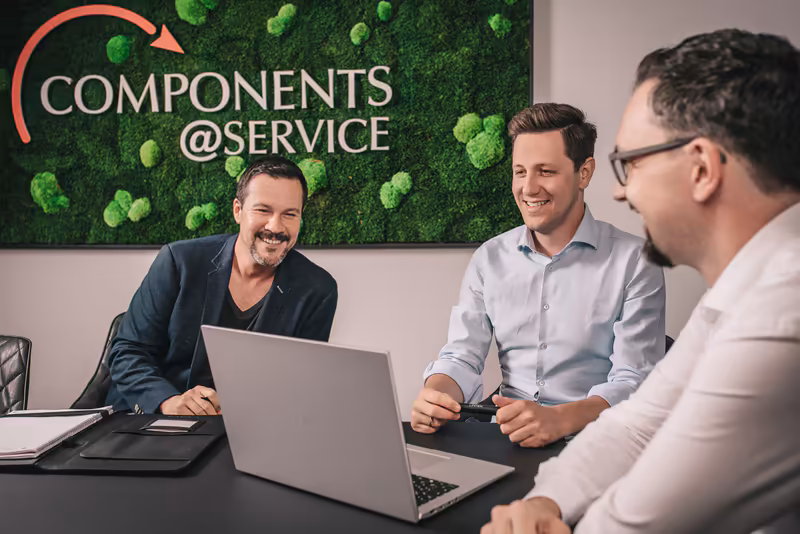 Drei Geschäftsmänner in Besprechung am Laptop, modernes Büro mit Mooswand und Components@Service Logo