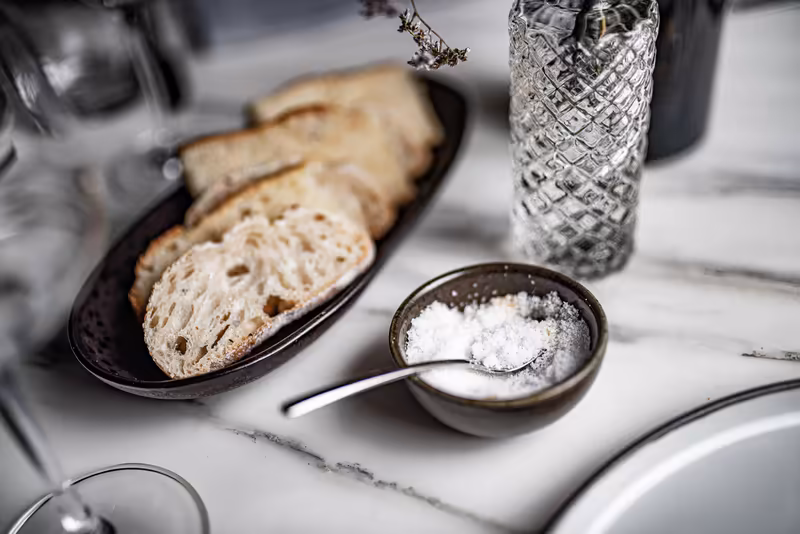 Elegantes Gedeck mit Brotscheiben, Salz und Wasserglas auf Marmortisch, gehobenes Dining-Setting