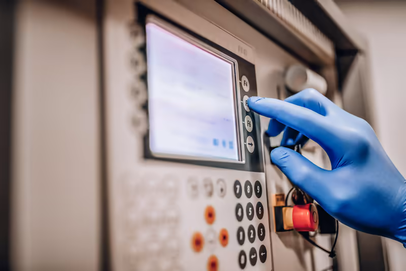 Hand in blauem Handschuh bedient Kontrolltafel mit Display in industrieller Umgebung