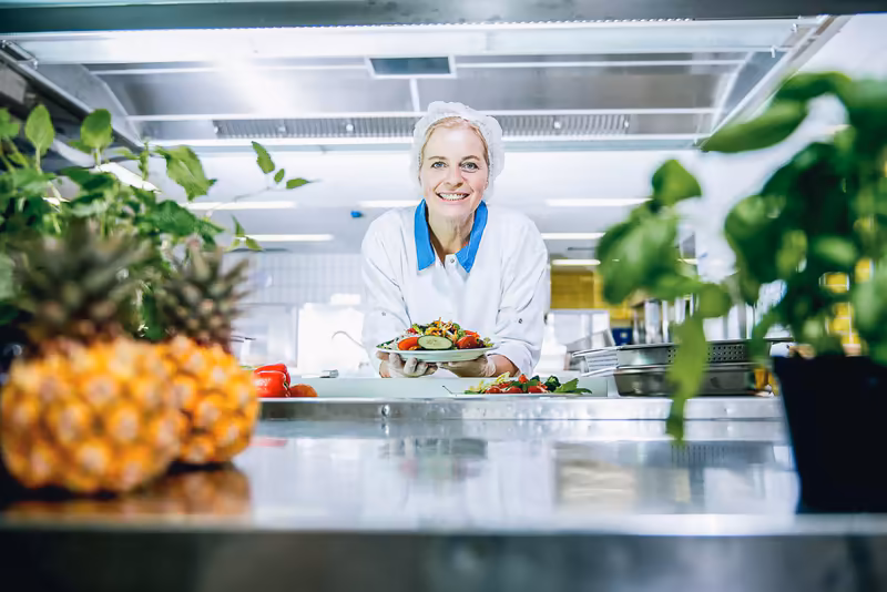 Ernährungsberaterin in moderner Küche präsentiert Salatgericht, umgeben von frischen Zutaten und Pflanzen