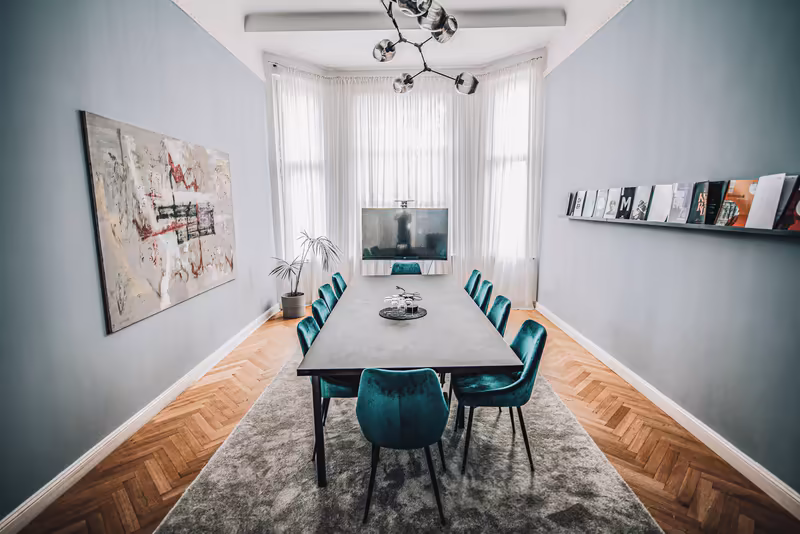 Modernes Besprechungszimmer mit grauem Konferenztisch, türkisen Samtsesseln und minimalistischer Einrichtung