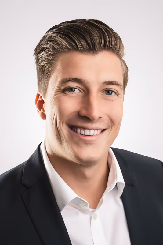 Mann im Business-Portrait, schwarzes Jacket, weißes Hemd, lächelnd, vor hellem Hintergrund