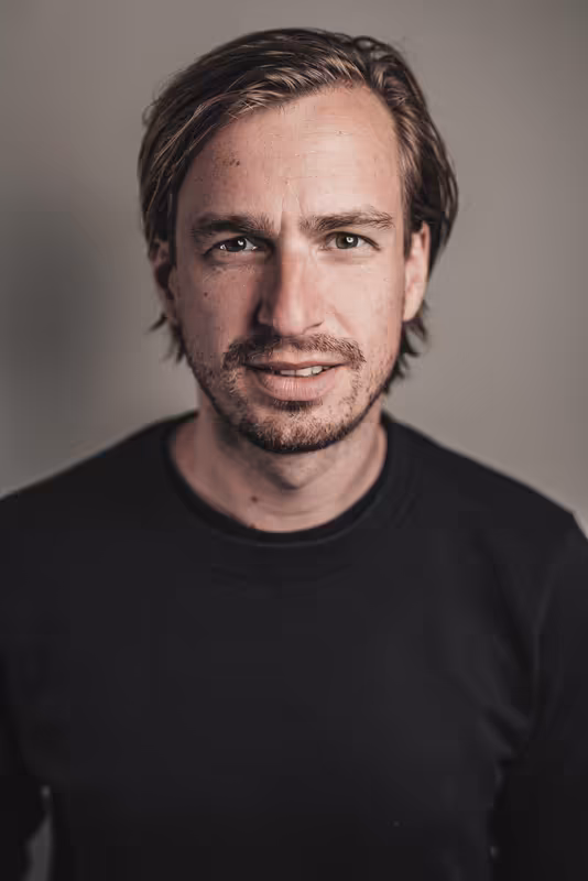 Mann mit dunklem Haar und Bart, schwarzes Shirt, neutraler Hintergrund, professionelles Porträt