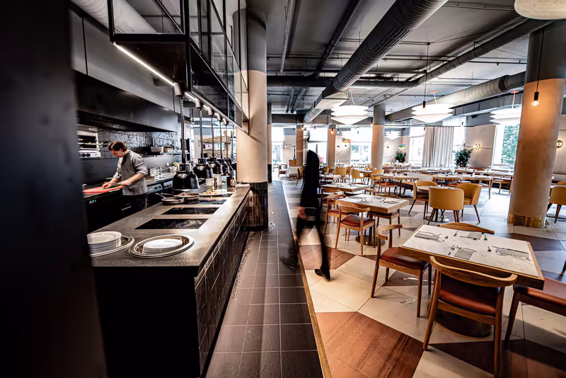 Modernes Restaurant-Interieur mit offener Küche, Mitarbeitern bei der Arbeit und Gastbereich mit Holzmöbeln