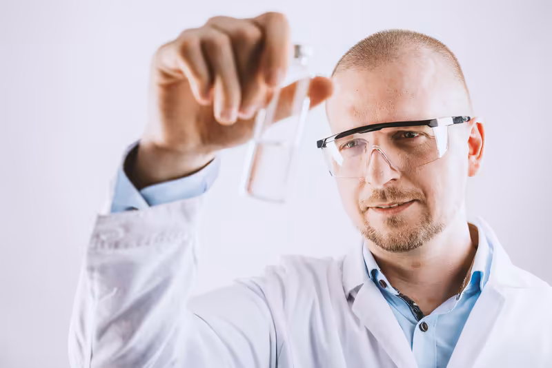 Wissenschaftler in Laborkittel und Schutzbrille hält Reagenzglas, konzentrierter Blick auf Experiment