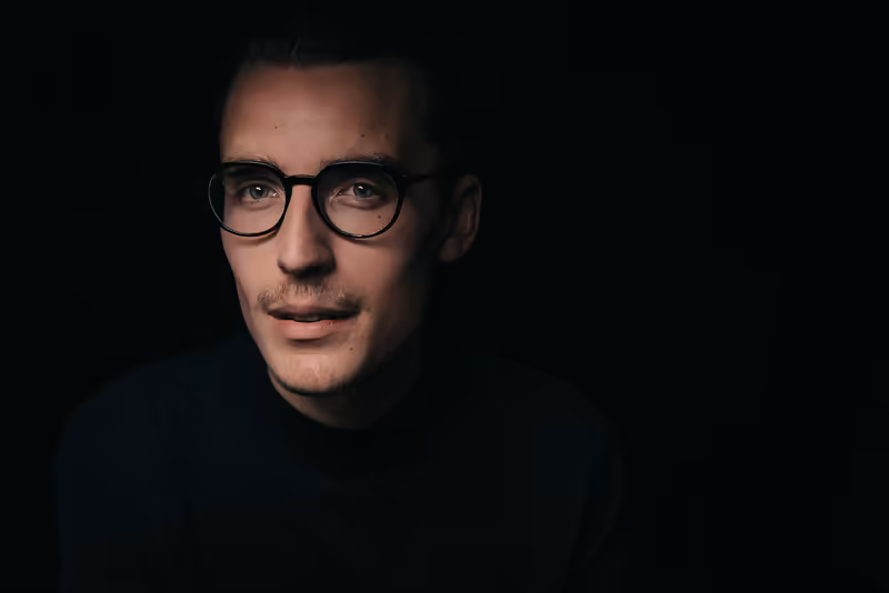Mann mit Brille, dunklem Hintergrund, professionelles Porträt, nachdenklicher Blick