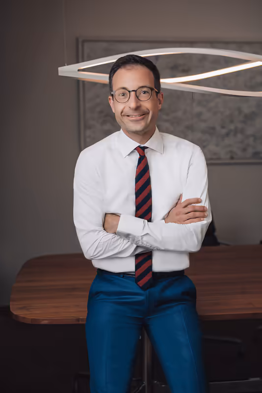 Mann in Business-Kleidung sitzt auf Schreibtisch, weiße Hemd, Krawatte, verschränkte Arme, modernes Büro-Setting
